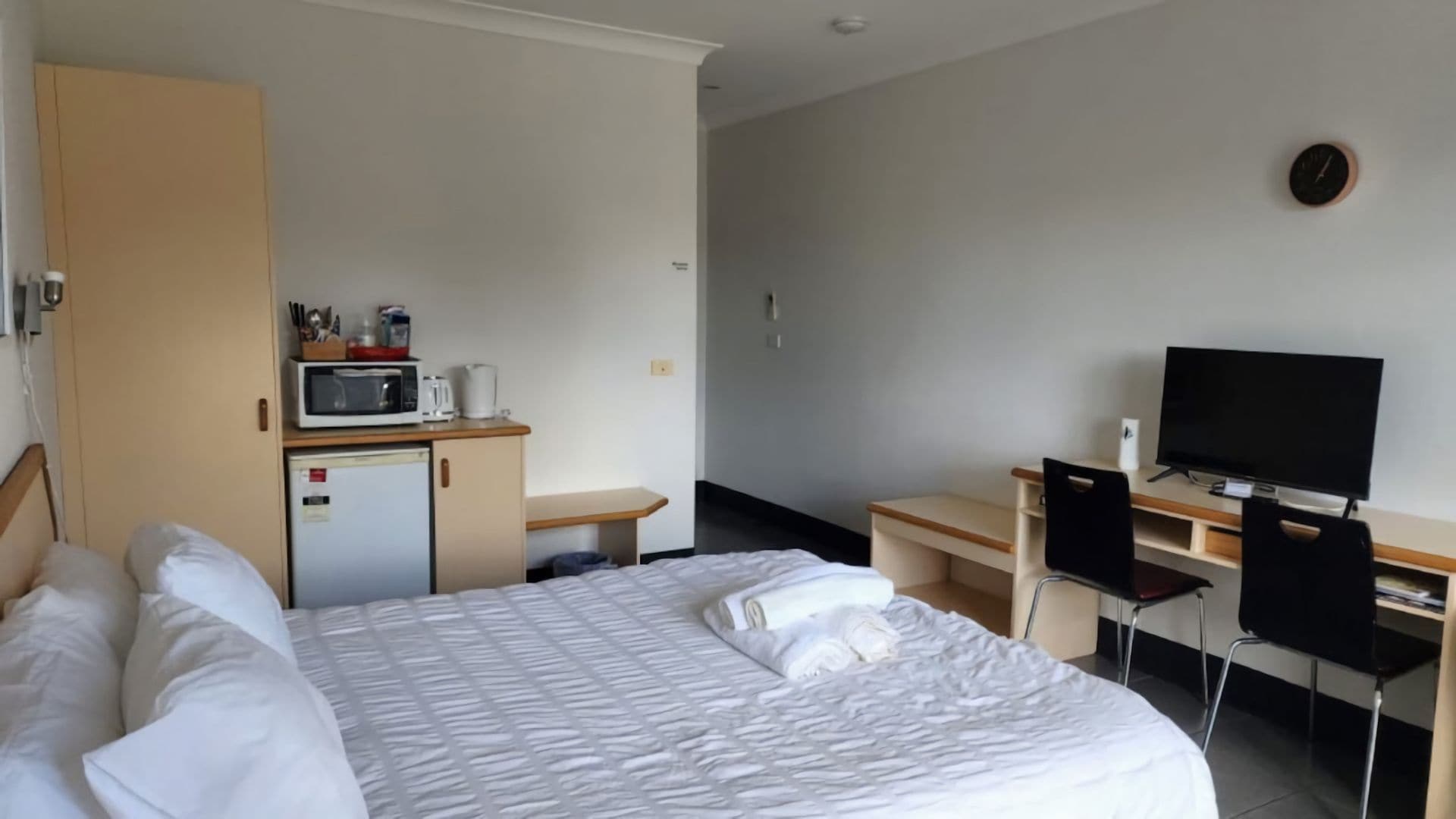 Ein Hotelzimmer mit Bett, Schreibtisch mit Stuhl, Fernseher, Mikrowelle und kleinem Kühlschrank.