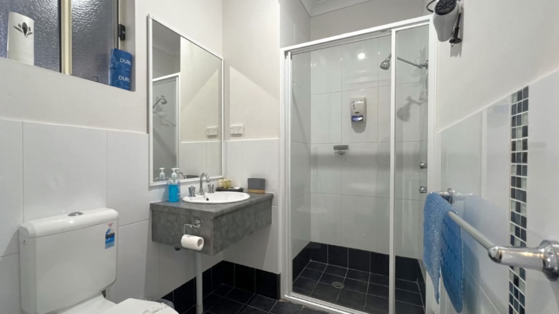A bathroom with a toilet, sink, mirror, and shower.
