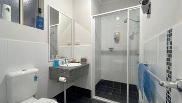 A bathroom with a toilet, sink, mirror, and shower.
