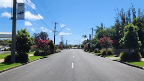 A road with a clear sky, power lines, and greenery on both sides.