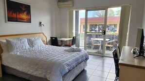 Une chambre d’hôtel avec un lit, un bureau, une chaise et un balcon donnant sur la rue.