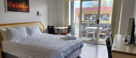 Ein Hotelzimmer mit Bett, Schreibtisch, Stuhl und einem Balkon mit Blick auf die Straße.