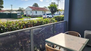 Ein Balkon mit Tisch und Stuhl, der auf eine Straße mit parkenden Autos und Häusern blickt.