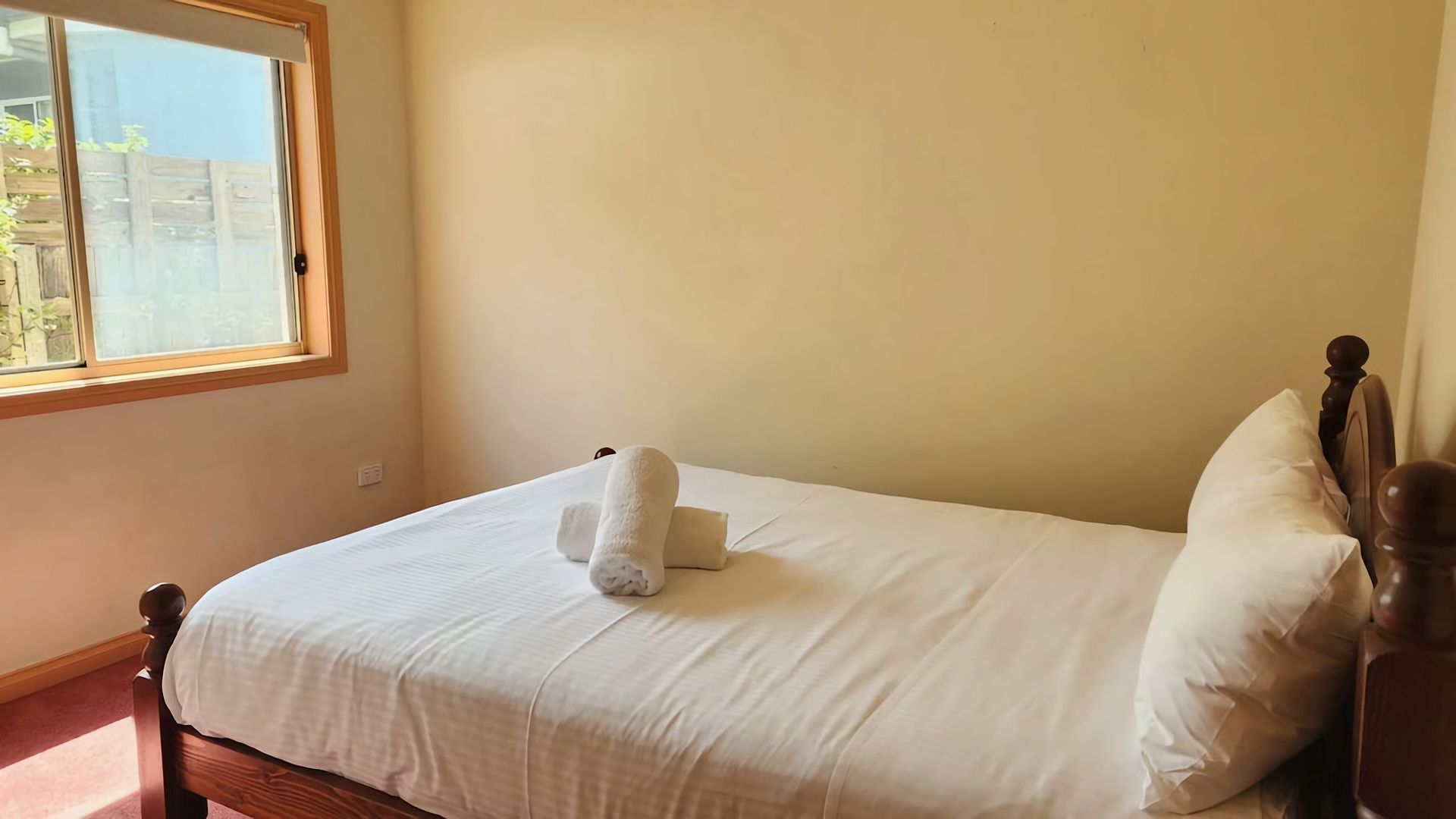 A single bed with white bedding and pillows, a wooden headboard, and a window with blinds.
