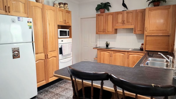 A kitchen with wooden cabinets, a refrigerator, a microwave, an oven, a sink, and two bar stools. - Sought After Location (Berrara)