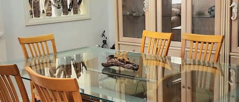 A dining area with a glass table surrounded by wooden chairs, a decorative piece on the table, and a cabinet with glass doors in the background.