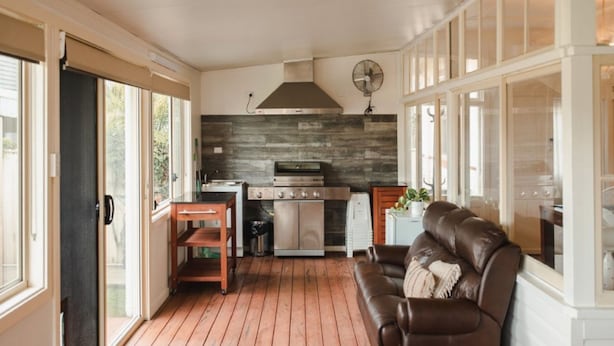 A kitchen with a stove, oven, and fan, a wooden dining table, and a brown leather couch.