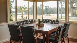 A dining area with a wooden table and chairs, large windows with a view of palm trees and a lake.