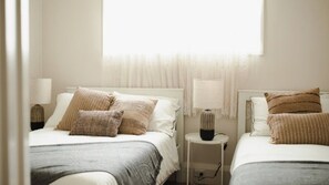 A hotel room with two beds, each with a bedside table and lamp.