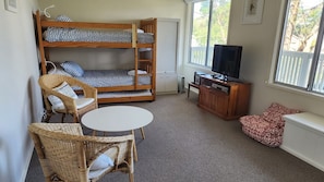 A room with a bunk bed, a television, a small table, wicker furniture, and a window with a view.