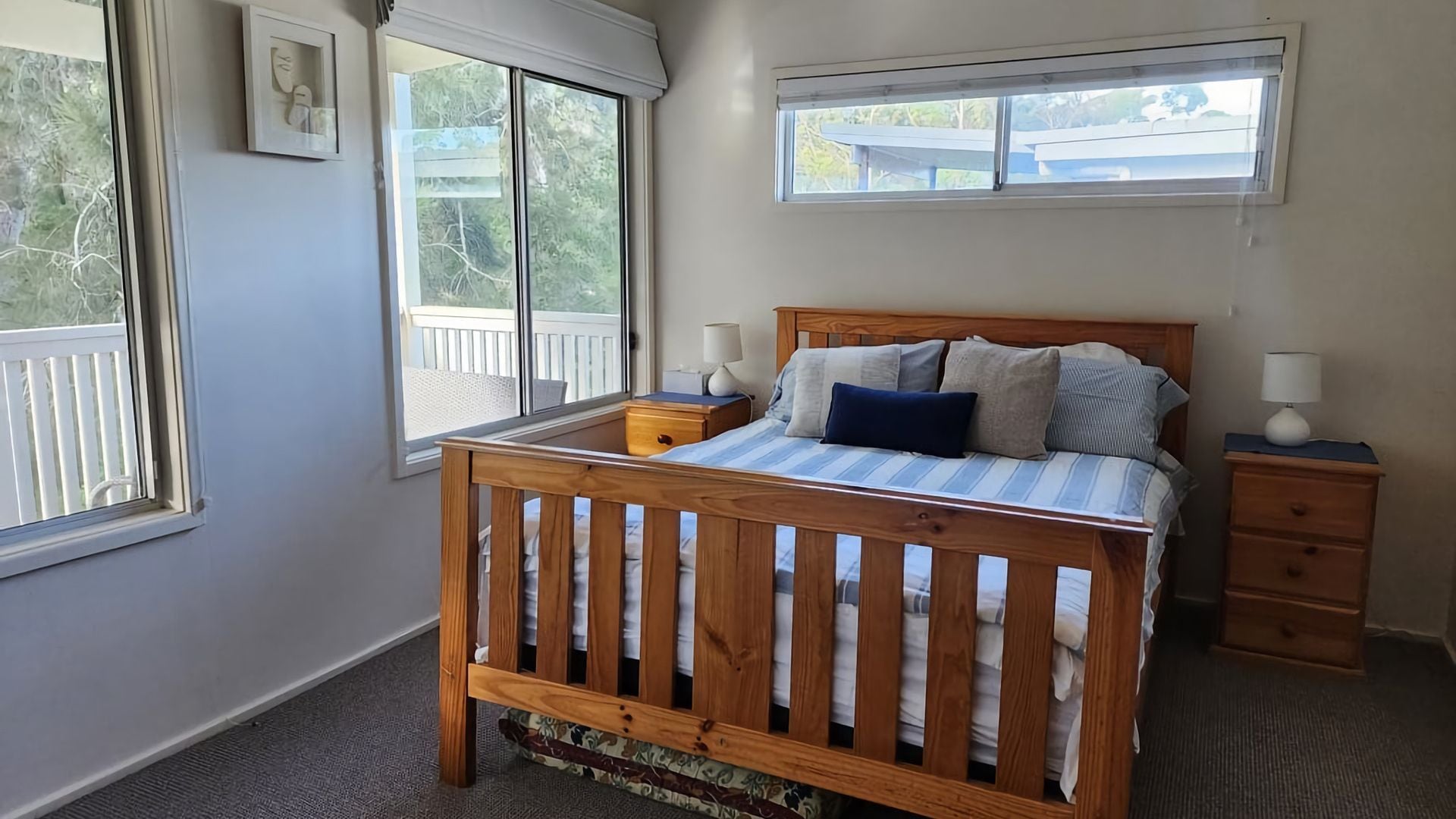 A bedroom with a wooden bed, two bedside tables, a window, and a view of a balcony.