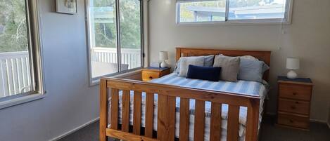 A bedroom with a wooden bed, two bedside tables, a window, and a view of a balcony.