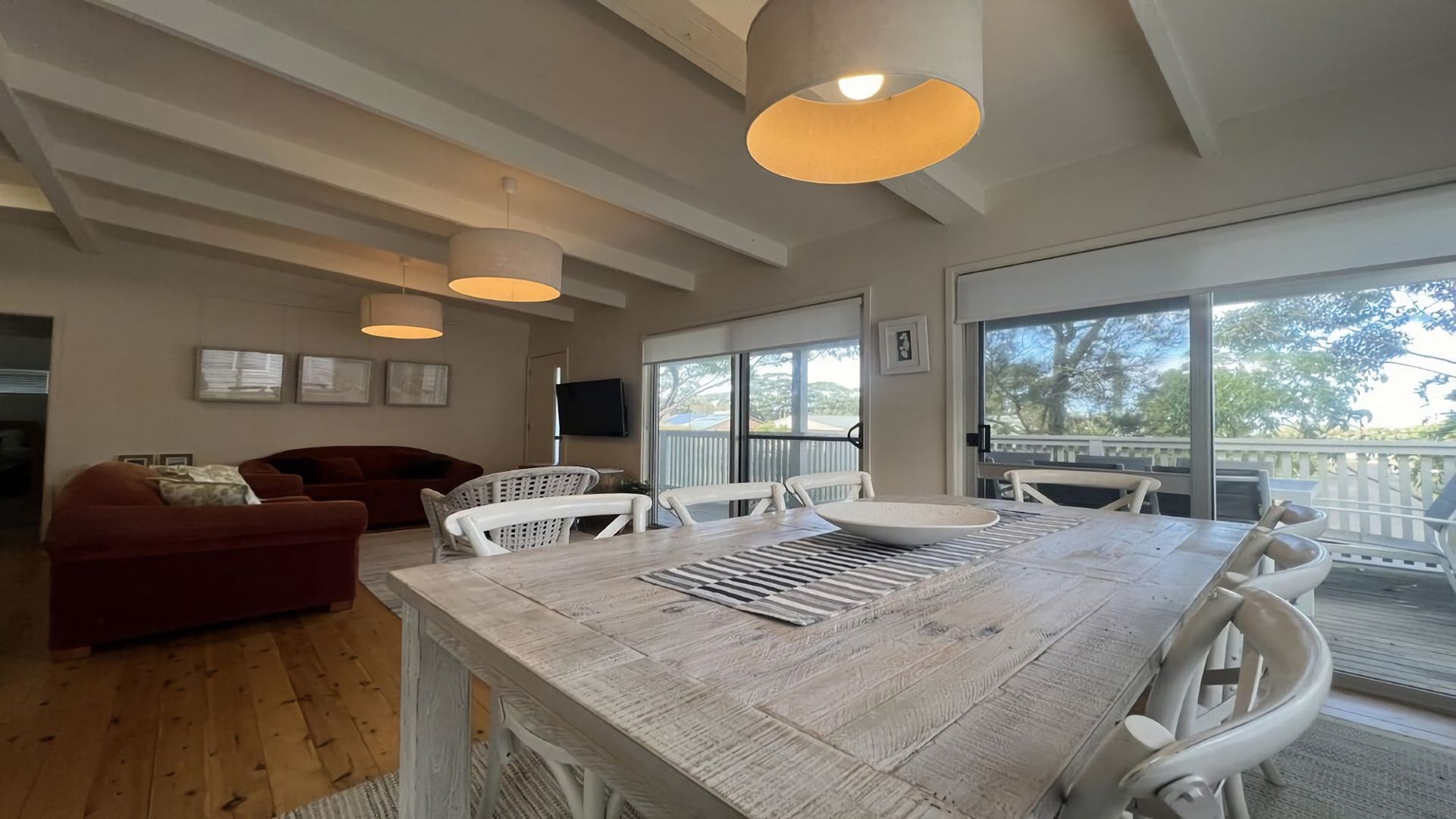 Un vaste espace de vie comprenant une grande table à manger en bois, des chaises blanches, un canapé rouge et un balcon avec vue.