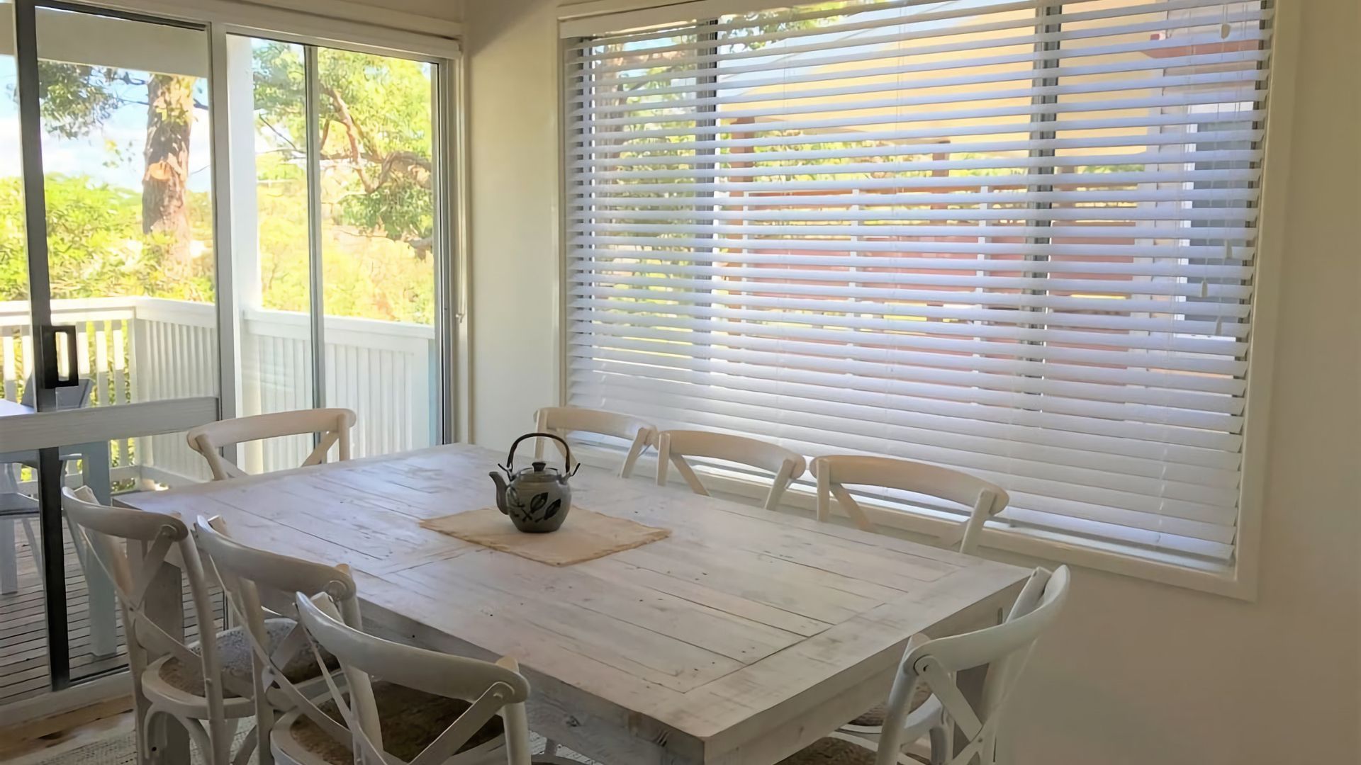 A dining area with a table and chairs, a window with blinds, and a view of a deck.