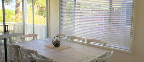 A dining area with a table and chairs, a window with blinds, and a view of a deck.
