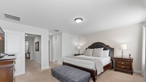 A bedroom with a large bed, a wooden nightstand, a bench, and a dresser. - Storey Lake Resort | 6BR Villa w/ Pool Near Disney (Kissimmee)