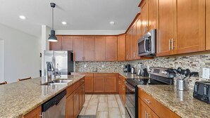 A modern kitchen with granite countertops, wooden cabinets, stainless steel appliances, and a backsplash with mosaic tiles. - Storey Lake Resort | 6BR Villa w/ Pool Near Disney (Kissimmee)