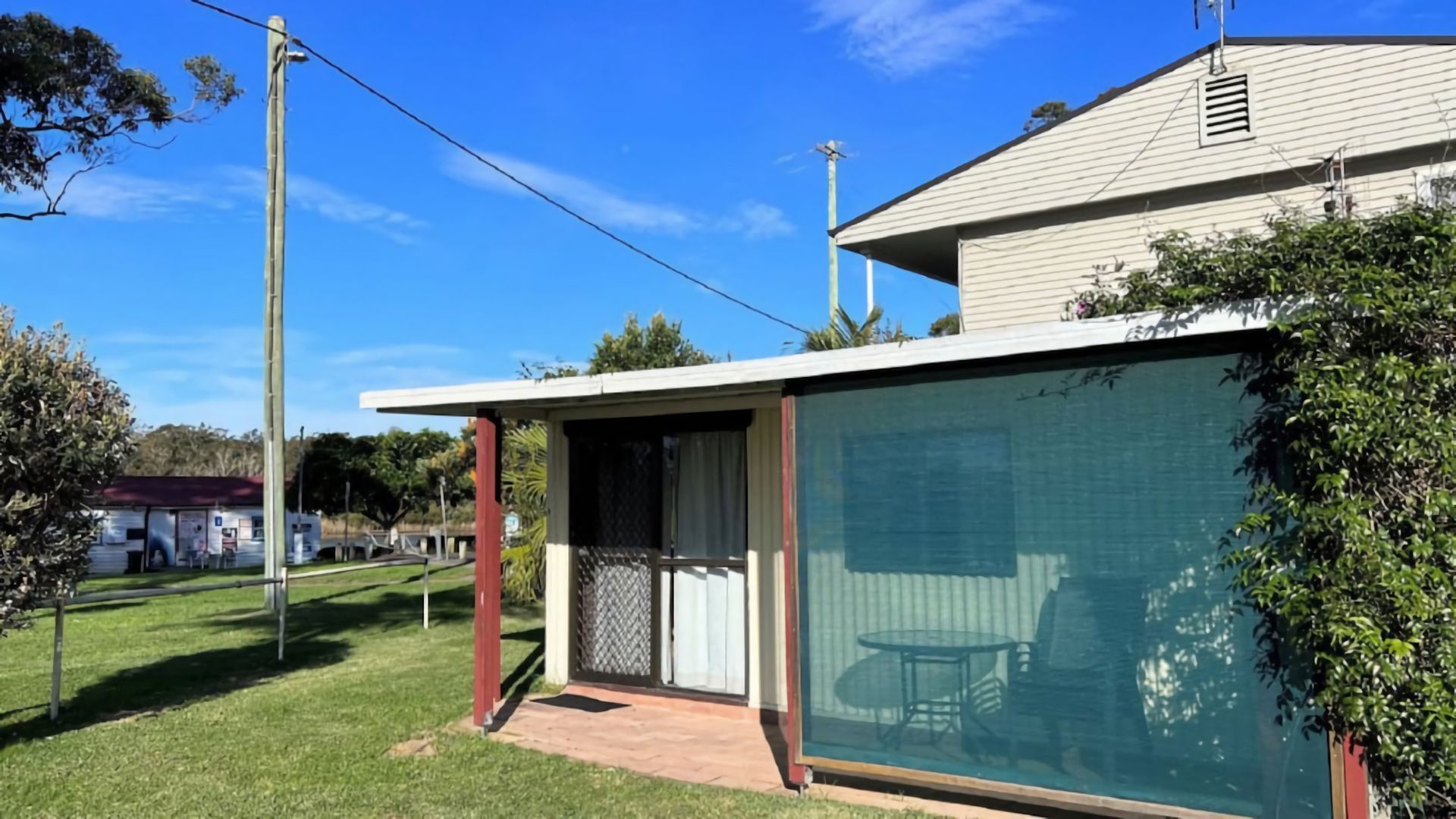 Ein Haus mit überdachter Terrasse, einem eingezäunten Garten und blauem Himmel.