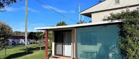 Ein Haus mit überdachter Terrasse, einem eingezäunten Garten und blauem Himmel.