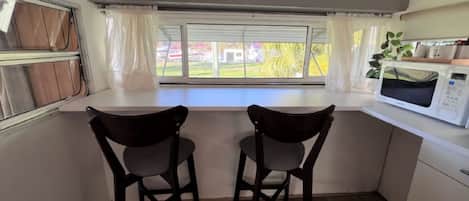 A kitchen with two chairs, a window with curtains, and a microwave.