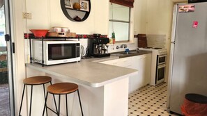 A kitchen with a microwave, coffee maker, and a stove. There are two stools and a sink.