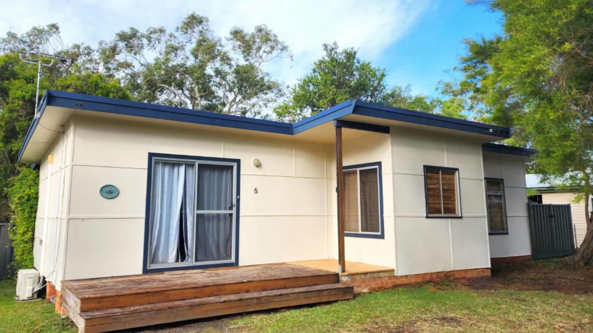 Une maison mobile de plain-pied, dotée d’un porche à l’avant, d’une porte-fenêtre coulissante et d’un petit jardin avant.