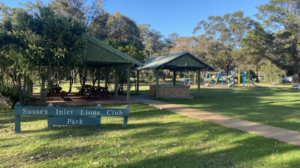 A park with picnic tables, a playground, and a sign for Sussex Inlet Lions Club Park.