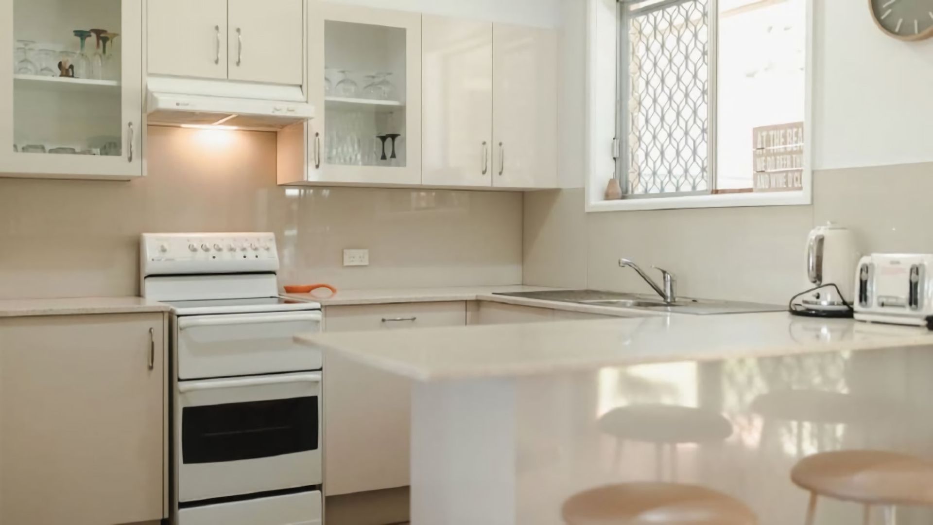 Una cocina con estufa, horno y pileta. Hay alacenas sobre la encimera y una ventana con un panel decorativo.