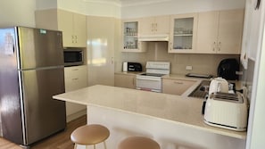 A compact kitchen with a refrigerator, microwave, toaster, and a bread maker. There are two stools and a sink.