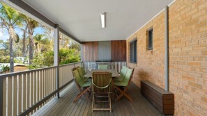 Un espace extérieur abrité, équipé d’une table et de chaises, d’un barbecue et offrant une vue sur la verdure.