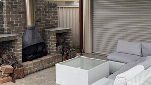Une terrasse avec une cheminée en briques, un canapé en osier blanc et une porte de garage fermée.