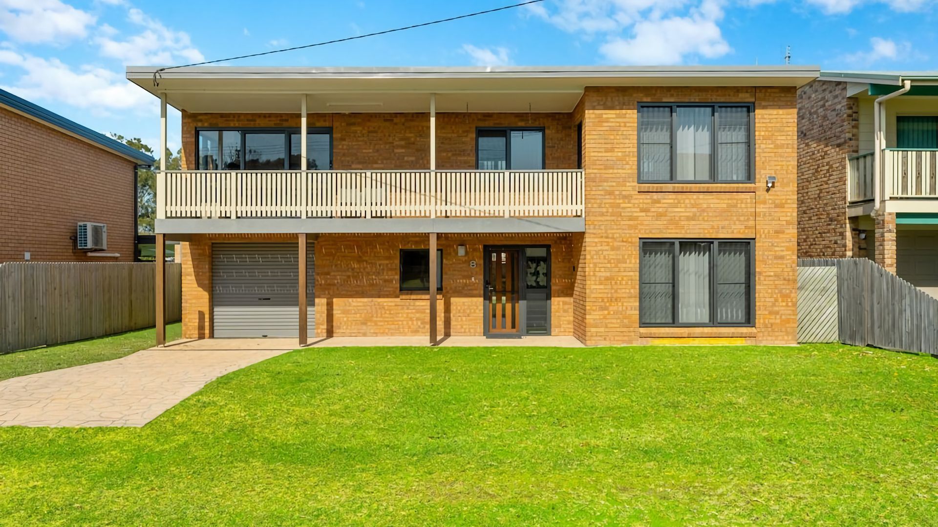 A two-story residential building with a flat roof, a balcony on the upper floor, and a front garage door.