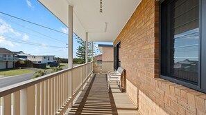 A covered balcony with a wooden floor, white railings, and a brick wall.