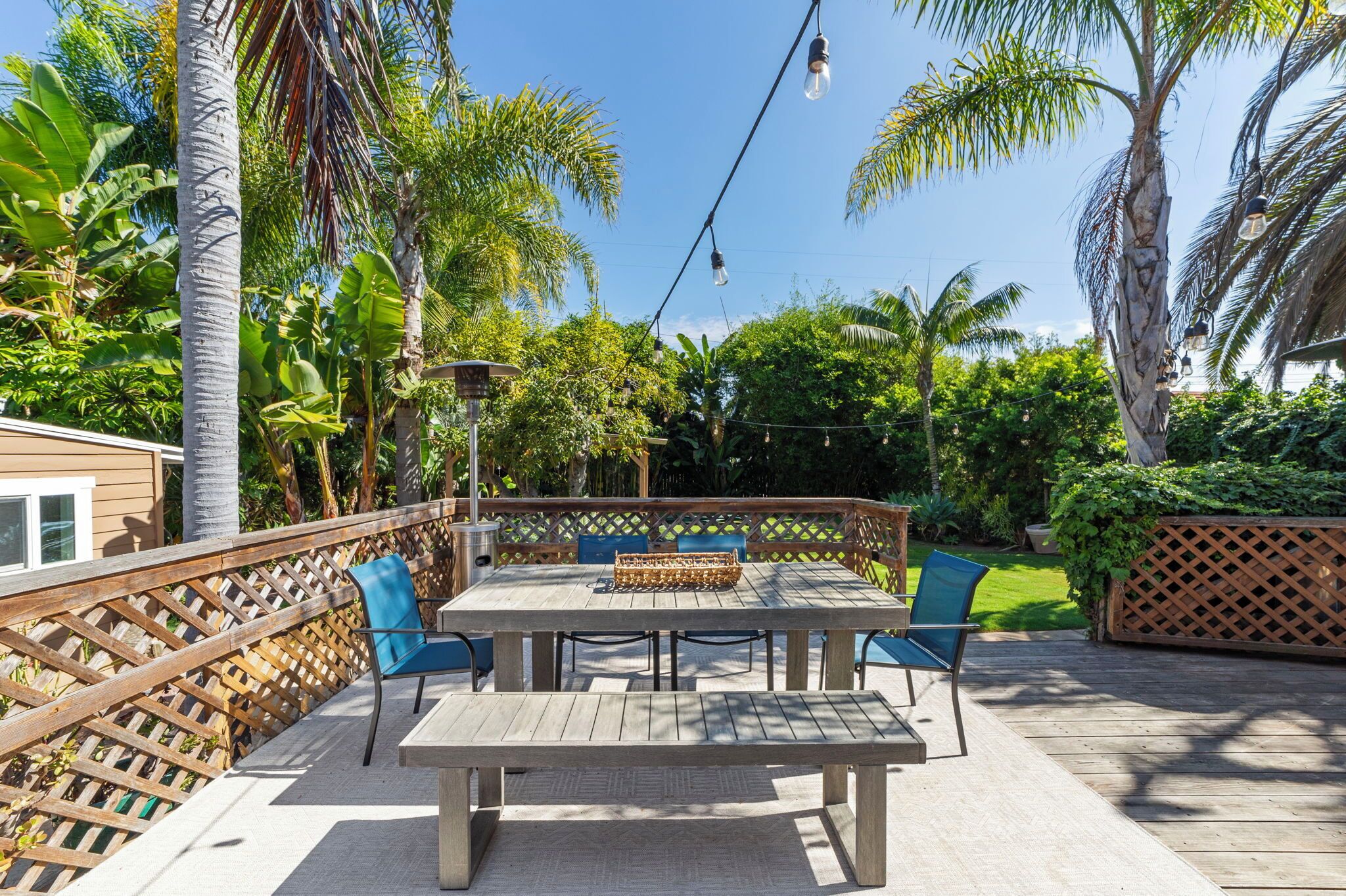 An outdoor patio with a wooden table and chairs, surrounded by a wooden fence and lush greenery.
