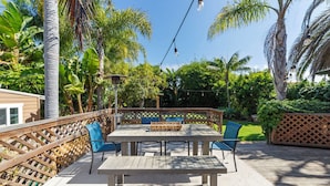 Un patio al aire libre con una mesa y sillas de madera, rodeado por una valla de madera y abundante vegetación.