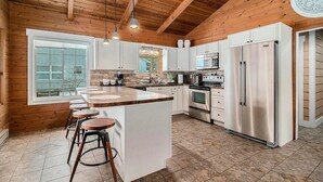 A modern kitchen with a large island, white cabinetry, stainless steel appliances, and a wooden ceiling.