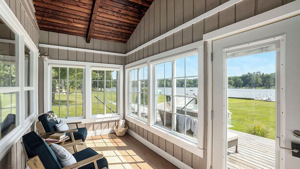 A sunroom with large windows, wooden ceiling, and a view of a lake.