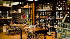 A cozy restaurant with wooden tables and chairs, a bookshelf filled with books and decorative items, and a patterned wall in the background.