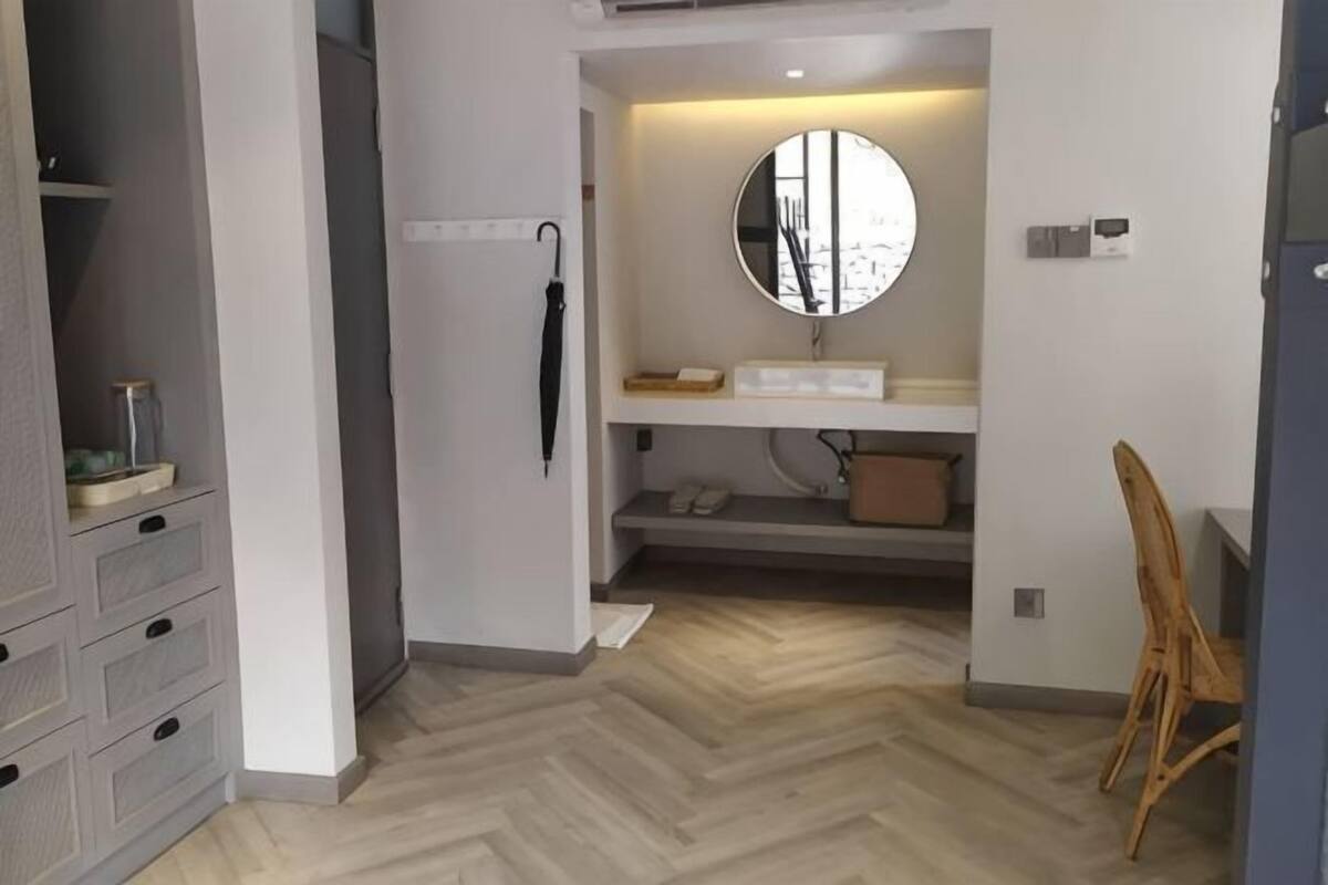 Une pièce avec un parquet en chevrons, un miroir rond au-dessus d’un lavabo, une chaise et une armoire à tiroirs.