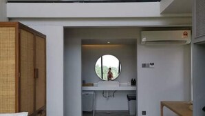 A modern bathroom with a round mirror, white sink, and a small stool.