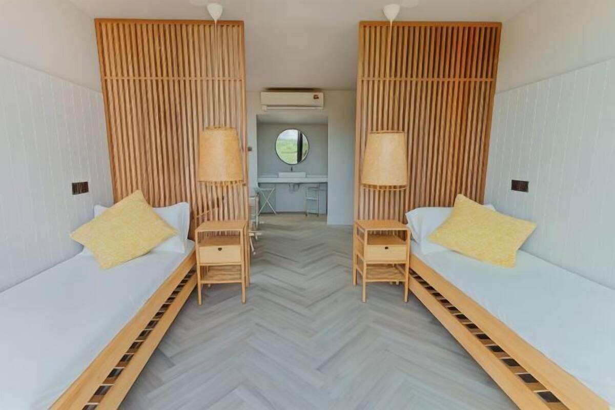 Une chambre avec deux lits, des têtes de lit en bois et un bureau central agrémenté d’un miroir.