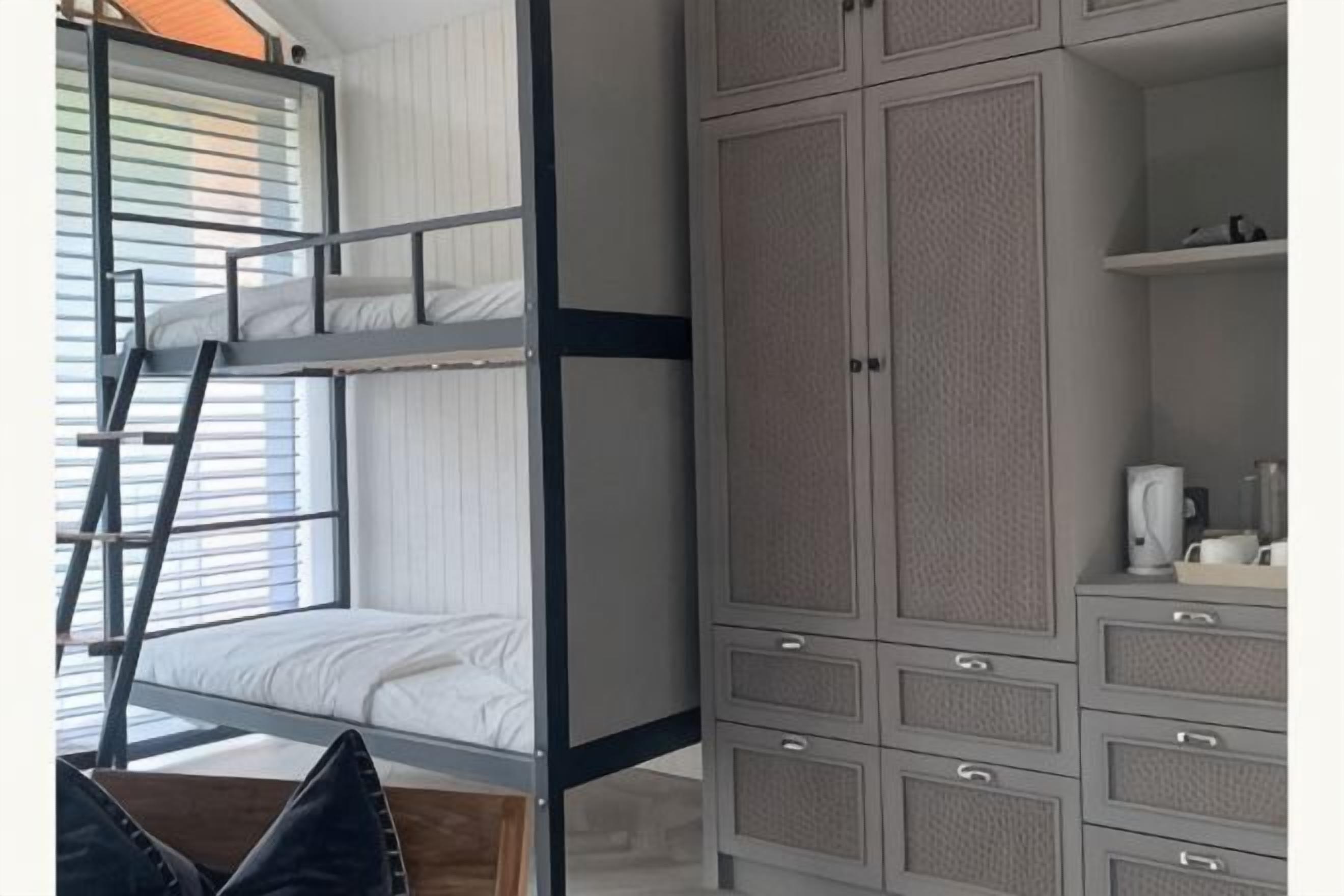 Een stapelbed met een ladder, een kledingkast met meerdere lades en een klein tafeltje met een waterkoker.