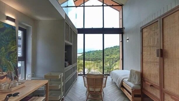 A room with a large window, a bed, a wooden chair, a desk, and a wardrobe.