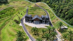 A large, modern building with a curved roof, surrounded by lush greenery and palm trees, with multiple access roads.