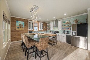 Una cocina moderna con paneles de madera, una isla central con taburetes de bar, electrodomésticos de acero inoxidable y una lámpara decorativa en el techo.