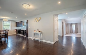 A spacious living room with hardwood flooring, a dining area with a wooden table and chairs, a kitchen with dark cabinets, and a white door leading to another room. - Lovely 4-bedroom house in Meriden (Meriden)