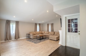 A spacious living room with a large L-shaped sectional sofa, a coffee table, and a door with a window. - Lovely 4-bedroom house in Meriden (Meriden)