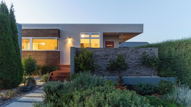 Une maison moderne avec un mur en pierre, une terrasse en bois et un jardin.