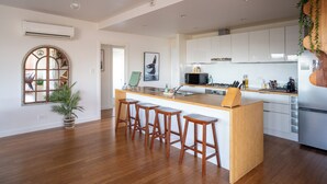 Une cuisine moderne avec des meubles blancs, un îlot central doté de tabourets et un four à micro-ondes encastré.