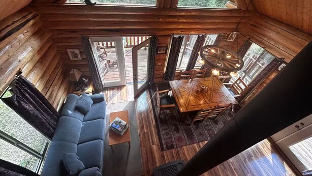 A cozy cabin interior with a wooden ceiling, a sofa, a dining table, and a view of the outdoors through large windows. - Lamar Valley Mountain Cabin (Silver Gate)